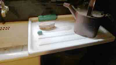 Old white enamel draining board, mounted against the sink on metal brackets.