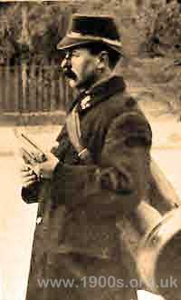 Side view of an early 1900s postman showing his dark blue uniform with its uniquely shaped hat and his special carrying bag.